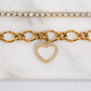 Gold bracelet with heart charm and clear gemstones on a white marble surface