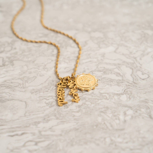 Gold necklace with charms on a textured beige surface