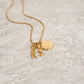 Gold necklace with charms on a textured beige surface
