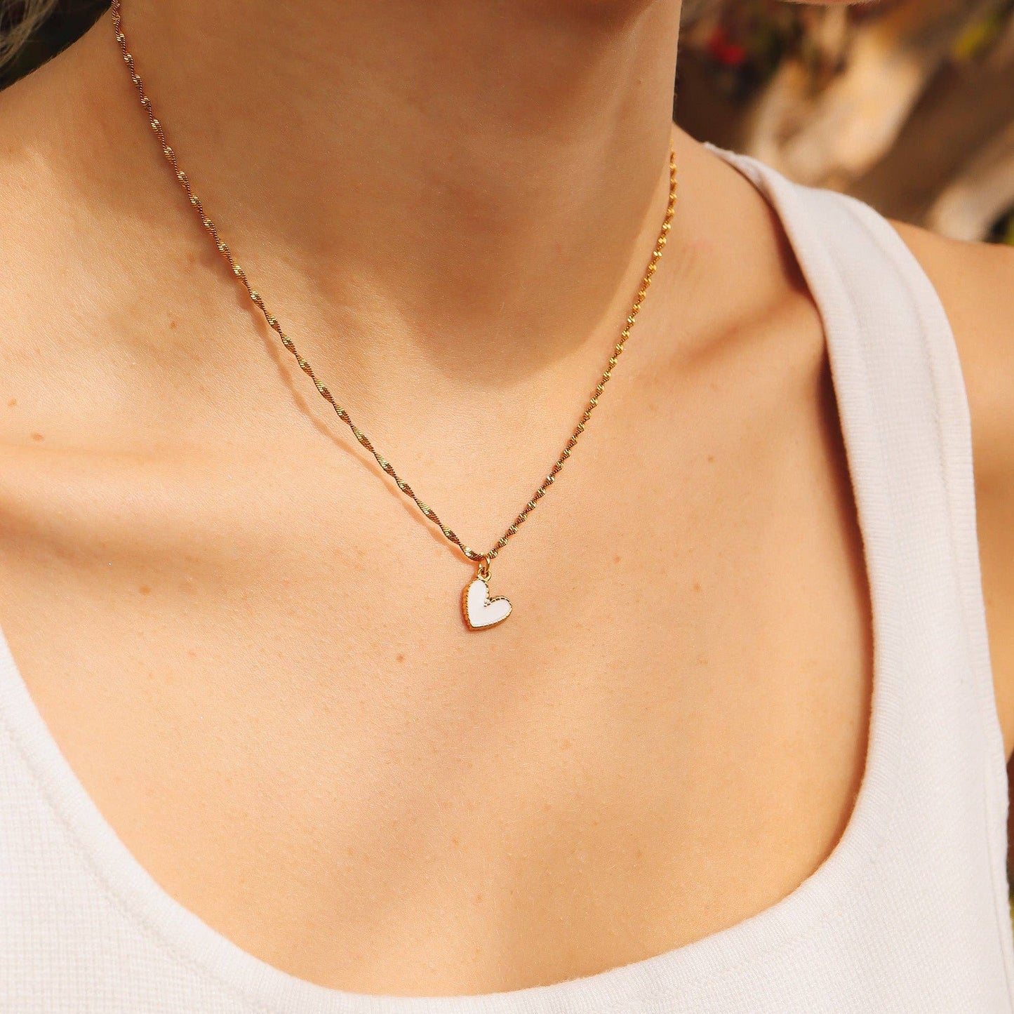Gold necklace with a heart pendant worn by a person in a white tank top