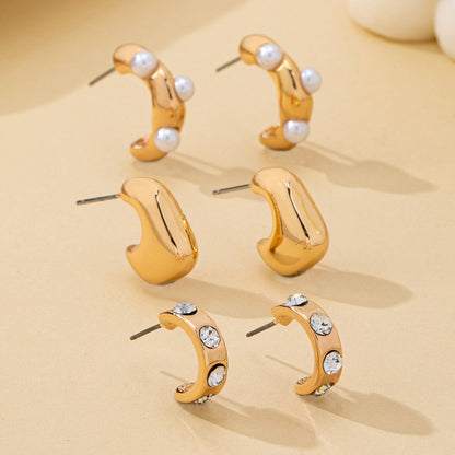 Set of gold hoop earrings with pearls and crystals on a beige background