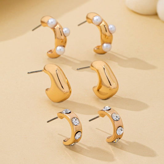 Set of gold hoop earrings with pearls and crystals on a beige background