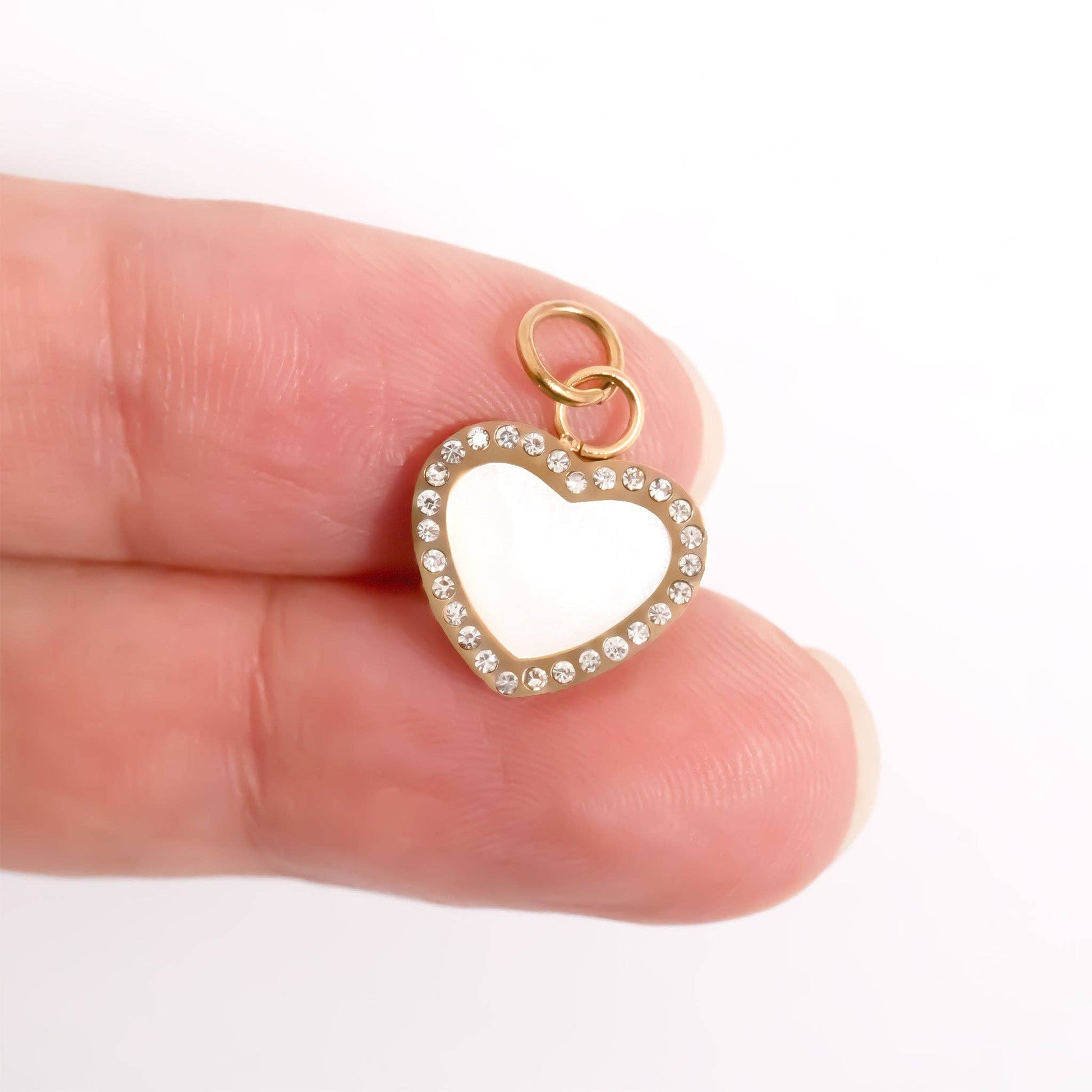 Gold heart-shaped pendant with clear stones held between fingers on a white background
