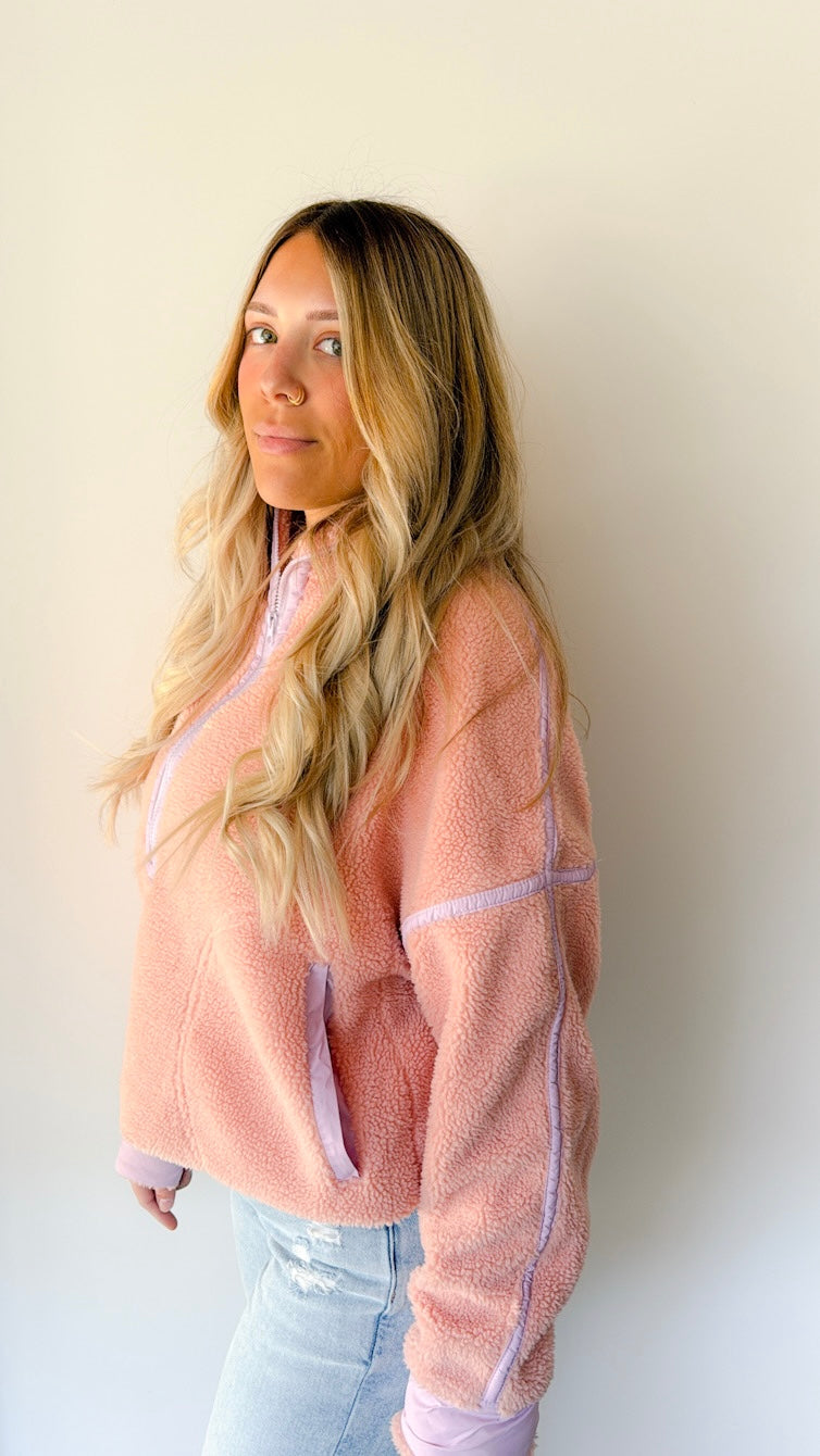 Model wearing a light pink and mauve Sherpa pullover by a white wall