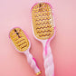 Pink and gold hairbrushes with decorative patterns on a pink background