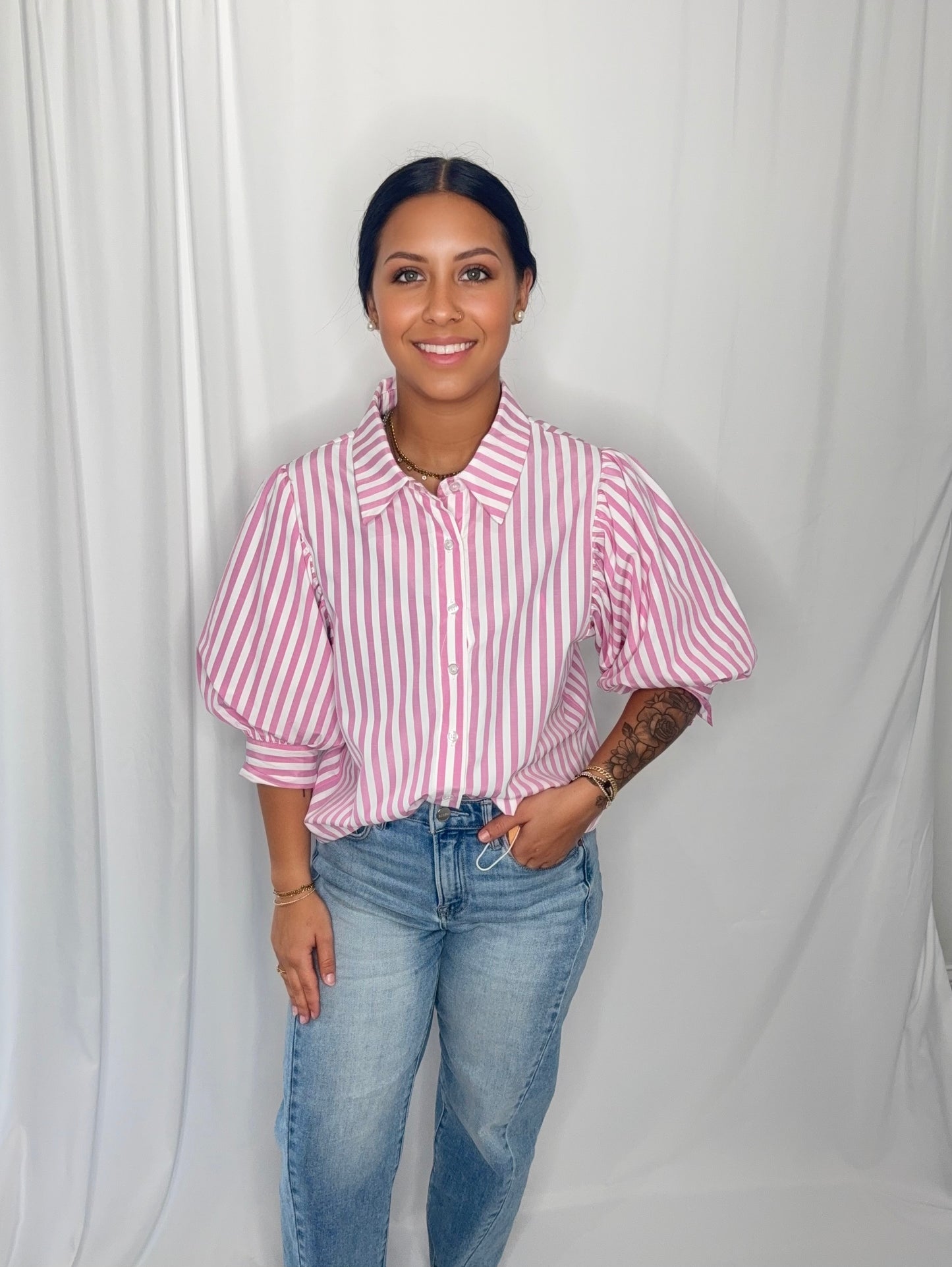 Woman wearing a pink and white striped shirt and blue jeans against a plain background