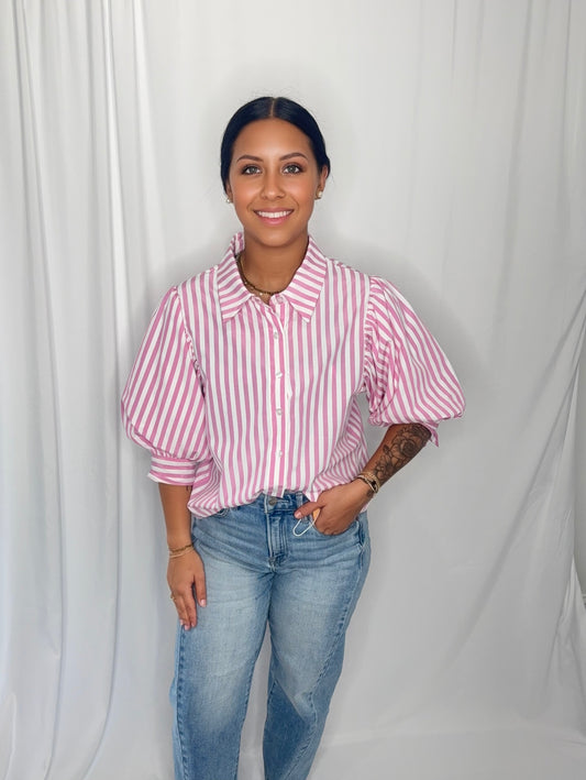 Woman wearing a pink and white striped shirt and blue jeans against a plain background