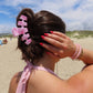 Person on a beach with pink hair clip and bracelet, wearing a pink top.