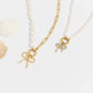 Two pearl necklaces with gold bow charms on a white background