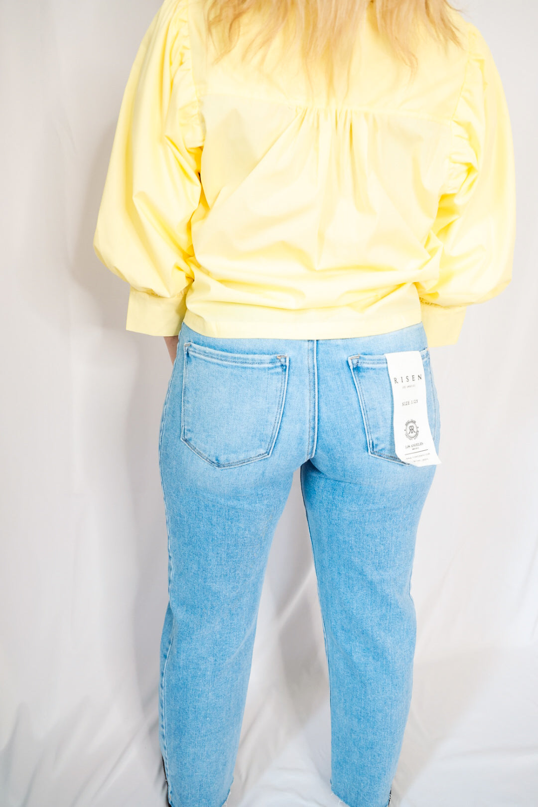 Person wearing a yellow sweatshirt and light blue jeans on a plain background