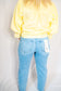 Person wearing a yellow sweatshirt and light blue jeans on a plain background