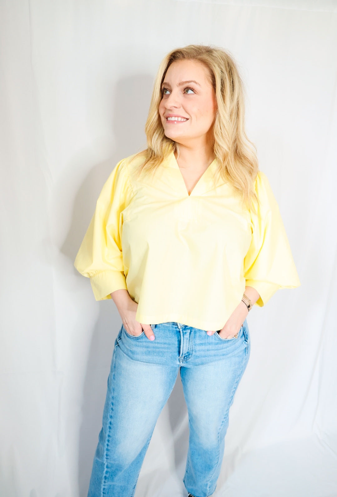 Woman wearing a yellow blouse and blue jeans against a plain background