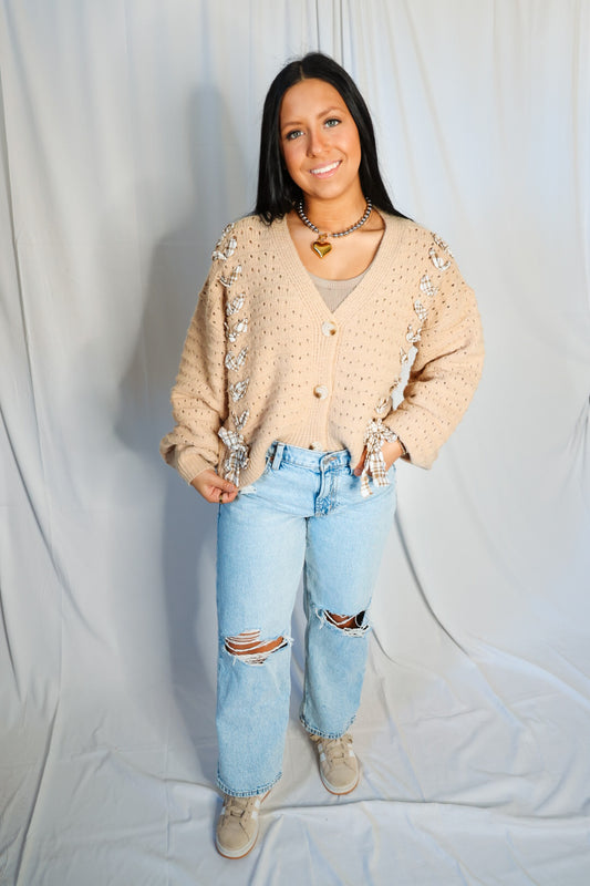 Person wearing a beige cardigan and light blue jeans against a plain background