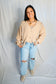 Person wearing a beige cardigan and light blue jeans against a plain background