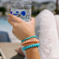 Hand holding a glass of water with a blurred outdoor background with 3 teleties hair ties on her hand