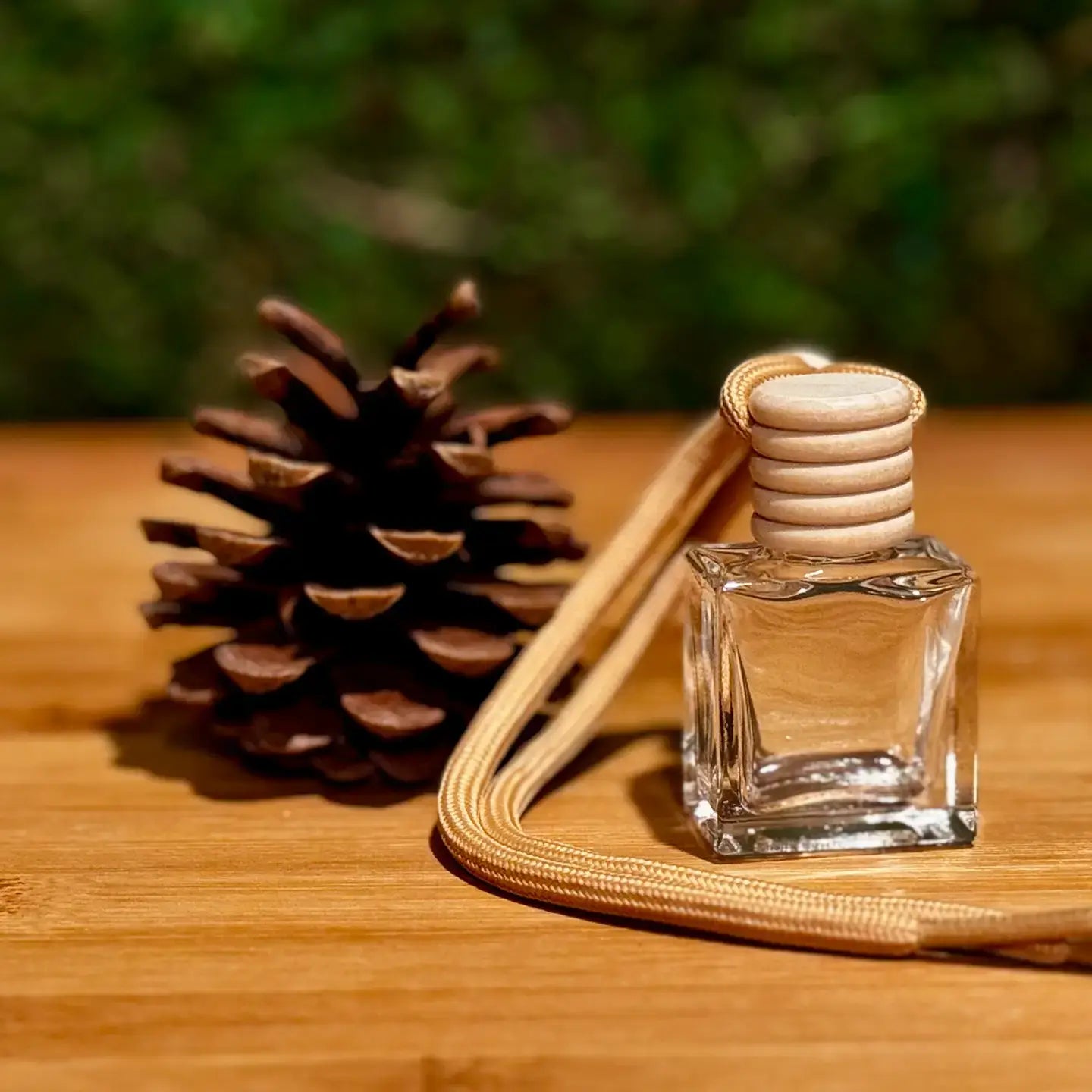 Clear glass diffuser bottle with wooden cap next to a pine cone on a wooden surface