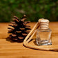 Clear glass diffuser bottle with wooden cap next to a pine cone on a wooden surface