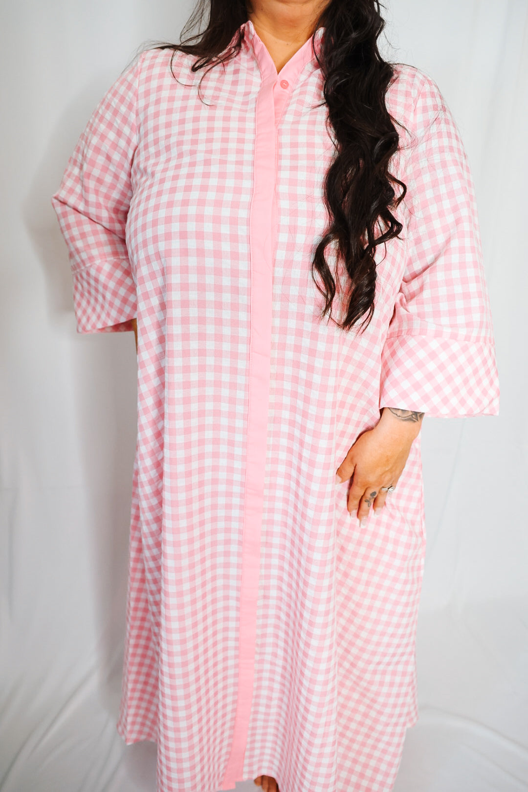 Person wearing a pink and white checkered dress against a plain background