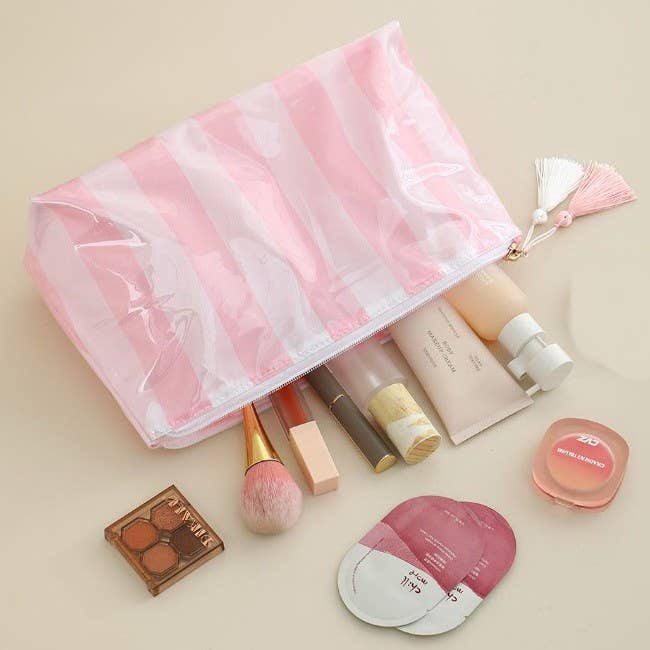 Makeup products including a pink brush, compact, and mirror on a beige surface with a pink mesh bag.