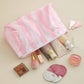 Makeup products including a pink brush, compact, and mirror on a beige surface with a pink mesh bag.