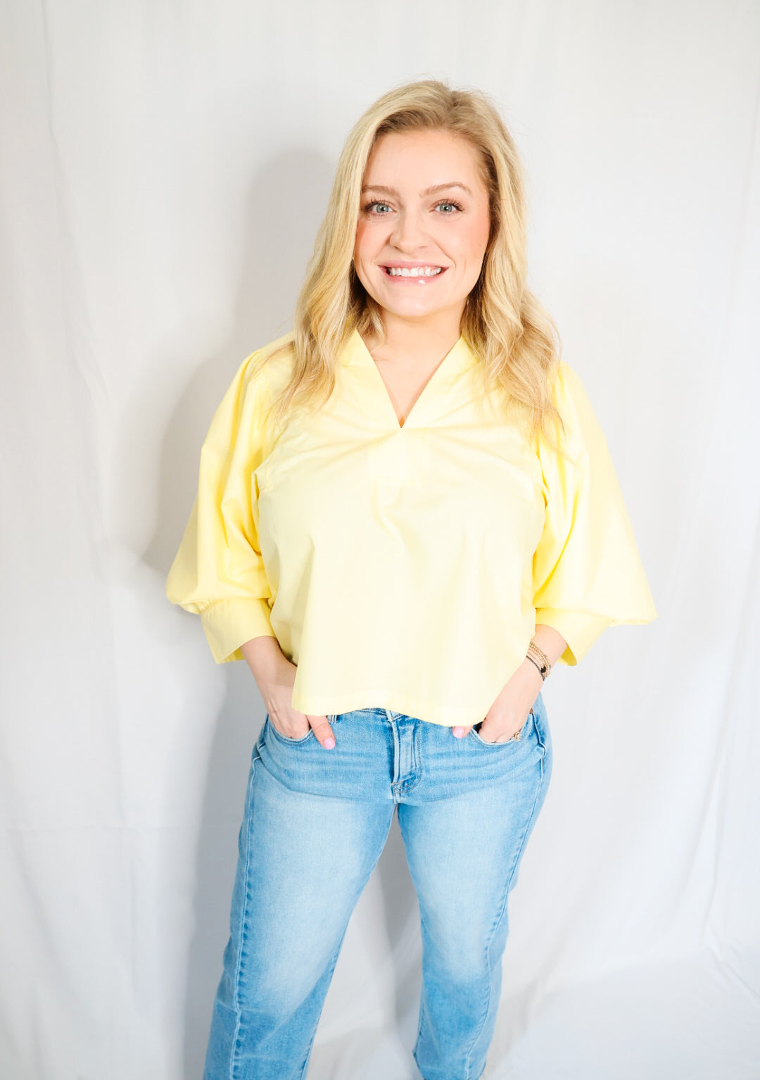 Woman wearing a yellow blouse and blue jeans against a plain background